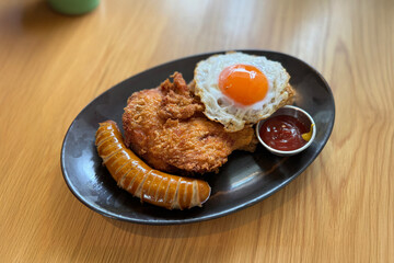 Delicious Fried Chicken with Sausage, Sunny-Side-Up Egg, and Dipping Sauce, Served on a Rustic Black Plate