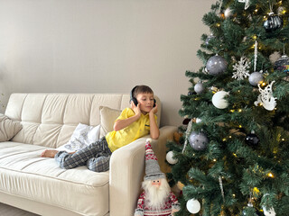 boy sitting on the sofa and listening to music on headphones, Christmas tree and anticipation of the holiday