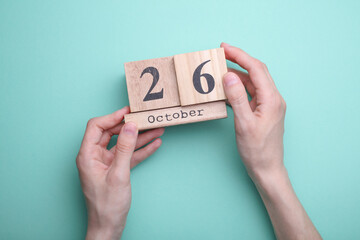 Hand holding wooden block calendar with date october 26 on mint green background