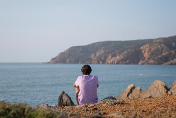 person sitting on the rocks watching the ocean and cliff at the beach in Cascais Portugal