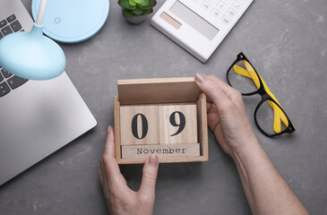 Hands holding a wooden block calendar 09 November against the background of a work space. Top view