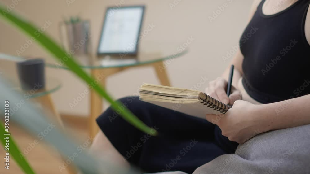 Poster a woman is sitting at a home office desk, writing in a notepad with a laptop in the background. she 