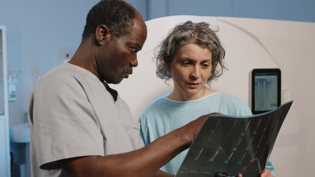 Black radiographer showing X-ray image to mature Caucasian female patient after CT scanning procedure