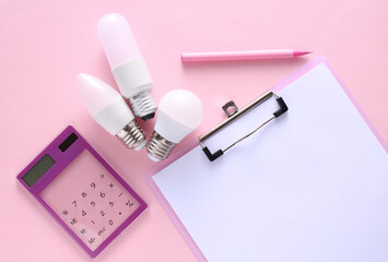 Energy efficiency. Calculator with energy-saving LED light bulbs and clipboard on a pink background