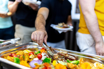 A group of friends enjoying a buffet meal at a casual gathering, savoring delicious dishes on a warm evening