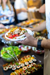 Enjoying a colorful buffet plate filled with grilled chicken and fresh vegetables at a lively event in a vibrant dining setting