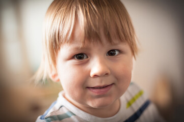 Young child smiling warmly in a cozy indoor setting during daylight, showcasing expressive eyes and playful demeanor