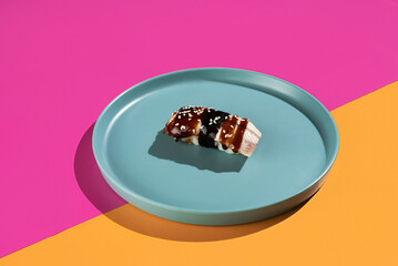 A plate of sushi sits on a blue plate with a pink background