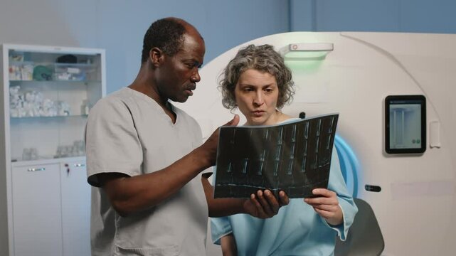 African American radiologist showing x-ray scan image to Caucasian woman after CT procedure