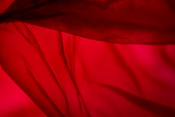 Extreme close up of red empty plastic bag background. The plastic surface is wrinkly and tattered making abstract pattern. Selective focus, shallow depth of field.
