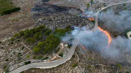 Aerial view of a fire in a countryside in Puglia, Italy. A road crosses the burned land.