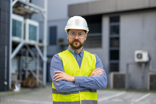 Confident construction worker wearing safety helmet and vest at industrial site, emphasizing safety and professionalism