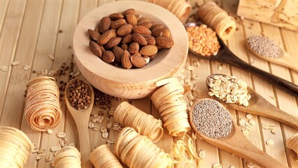 Wooden spoons and bowl holding organic ingredients like almonds, oats, chia seeds, buckwheat in natural setting. Minimalist design focusing on sustainability food choices Organic wood