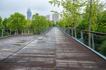 An elevated wooden boardwalk or footbridge in an urban public park leads to some modern residential...