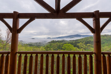 Fototapeta premium A stunning view of the mist-covered Smoky Mountains as seen from a rustic cabin balcony, framed by timber beams. Perfect depiction of nature and tranquility
