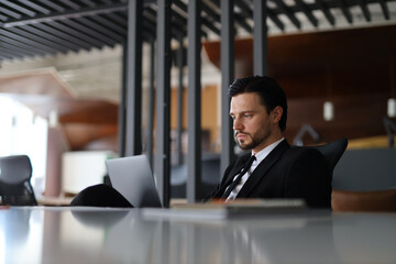 A man in a suit is sitting at a desk with a laptop open. He is focused on his work, possibly typing or browsing the internet. Concept of professionalism and productivity