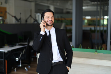 A man in a suit is talking on his cell phone. He is smiling and he is in a good mood