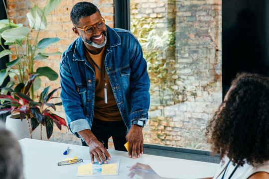 Smiling business owner in a stylish denim jacket leads a meeting in a bright, airy office space