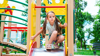happy preschooler girl playing on a slide on the playground in summer