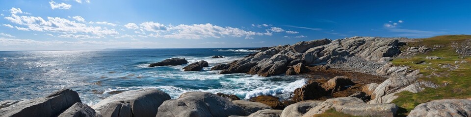 Obraz premium A beautiful ocean view with a rocky shoreline. The sky is clear and blue, and the water is calm. The rocks are scattered along the shoreline, and the grass is growing on the hillside