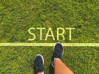 Women's feet are standing on green grass with the word “start” written on it. A novice...