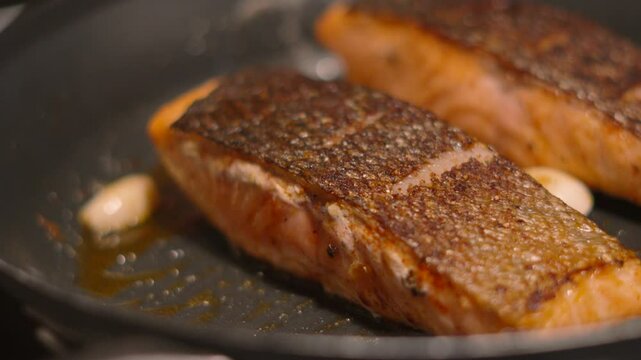 Salmon Fish Fillets Cooking in Frying Pan with Crispy Skin with Oil, Butter and Garlic Cloves. Food Preparation Ready to Serve Lunch or Dinner 4K