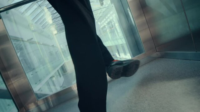 Freaky businessman in white turtleneck, black suit and red socks making bizarre dancing performance in silver elevator with glass wall in modern indoor office space