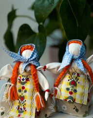 Two traditional Ukrainian motanka dolls with light blue headscarves and two long red braids each,...