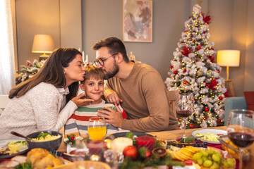 Parents kissing child while having Christmas dinner at home