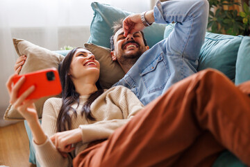 Couple having fun while relaxing at home using smart phone