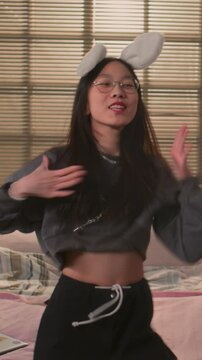 Vertical view of Asian girl dancing to k-pop song and lip syncing while recording trending video at home