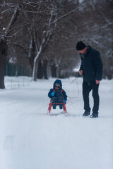 Grandfather and a little boy sledging, having fun on cold winter day.