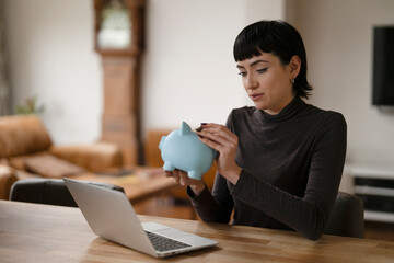 Young Woman Managing Finances While Holding Blue Piggy Bank at Home During a Quiet Afternoon