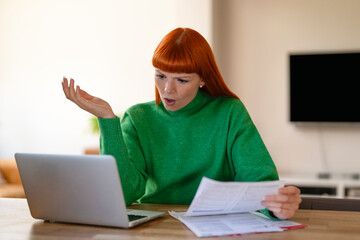 Frustrated Woman in Green Sweater Reacts to Unexpected Bills While Working on Her Laptop at Home