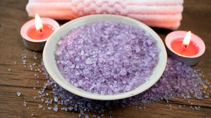 Arrangement of purple crystals of natural sea salt on a wooden table, next to two lighted candles.