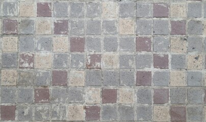 Image of a walkway made of alternating red, grey and cream stones. Stone pavement texture. The road is paved with square stones.