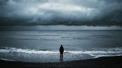 A solitary figure stands by a dark beach under a stormy sky, creating an atmosphere of introspection and solitude.