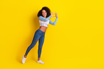 Full size photo of nice good mood girl dressed stylish shirt jeans fingers showing heart symbol isolated on yellow color background