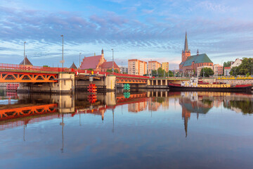 Fototapeta premium Morning view of a bridge and St James Cathedral in Szczecin, Poland, with clear reflections in the calm waters of the Oder River, framed by the city's architecture