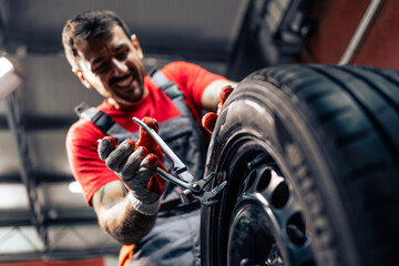 Hardworking tire technician adding weigh and balancing car wheels.