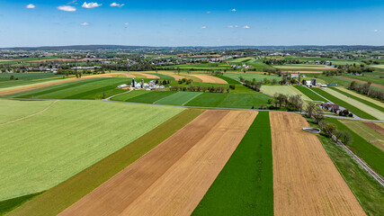 Vibrant green and brown fields intersperse across a picturesque countryside. Farms and rural roads are visible under a bright blue sky, showcasing early spring beauty.