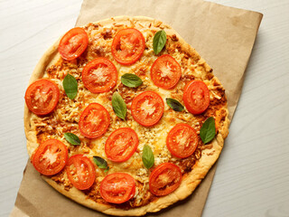 Whole margherita pizza on rustic paper and on a blurred wooden background with space for text
