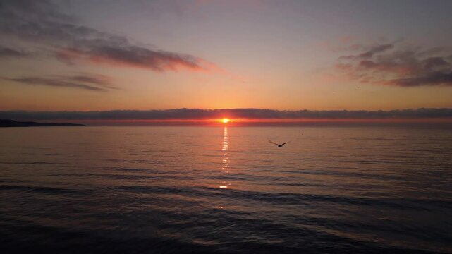 A tranquil drone shot of a stunning sunrise over calm ocean waters, with a peaceful horizon and subtle clouds reflecting warm golden tones
