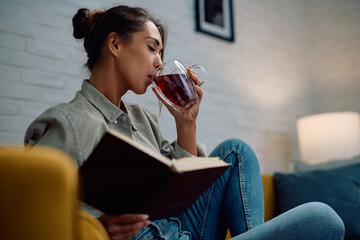 Young woman having a cup of tea while reading book at home.