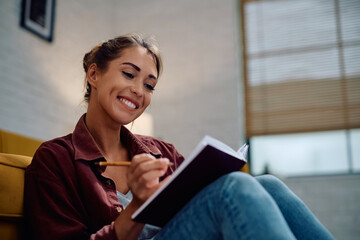 Young happy woman writing in notebook at home.
