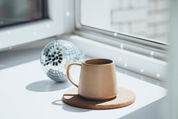 A cup and disco ball on the windowsill reflecting the light.