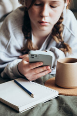 A teenage girl uses smartphone is drawing or doing homework in the bedroom.