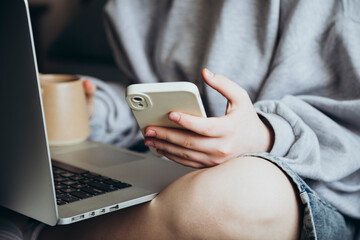 Young girl studies on the bed using computer and smartphone, close up.