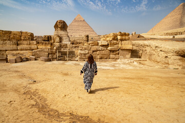 A rear view of a woman in a long traditional Muslim dress looking at the 3 great Pyramids in Egypt