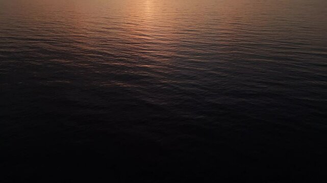 A minimalist drone shot capturing the soft reflections of a sunset on calm ocean waters, evoking a sense of peace and tranquility